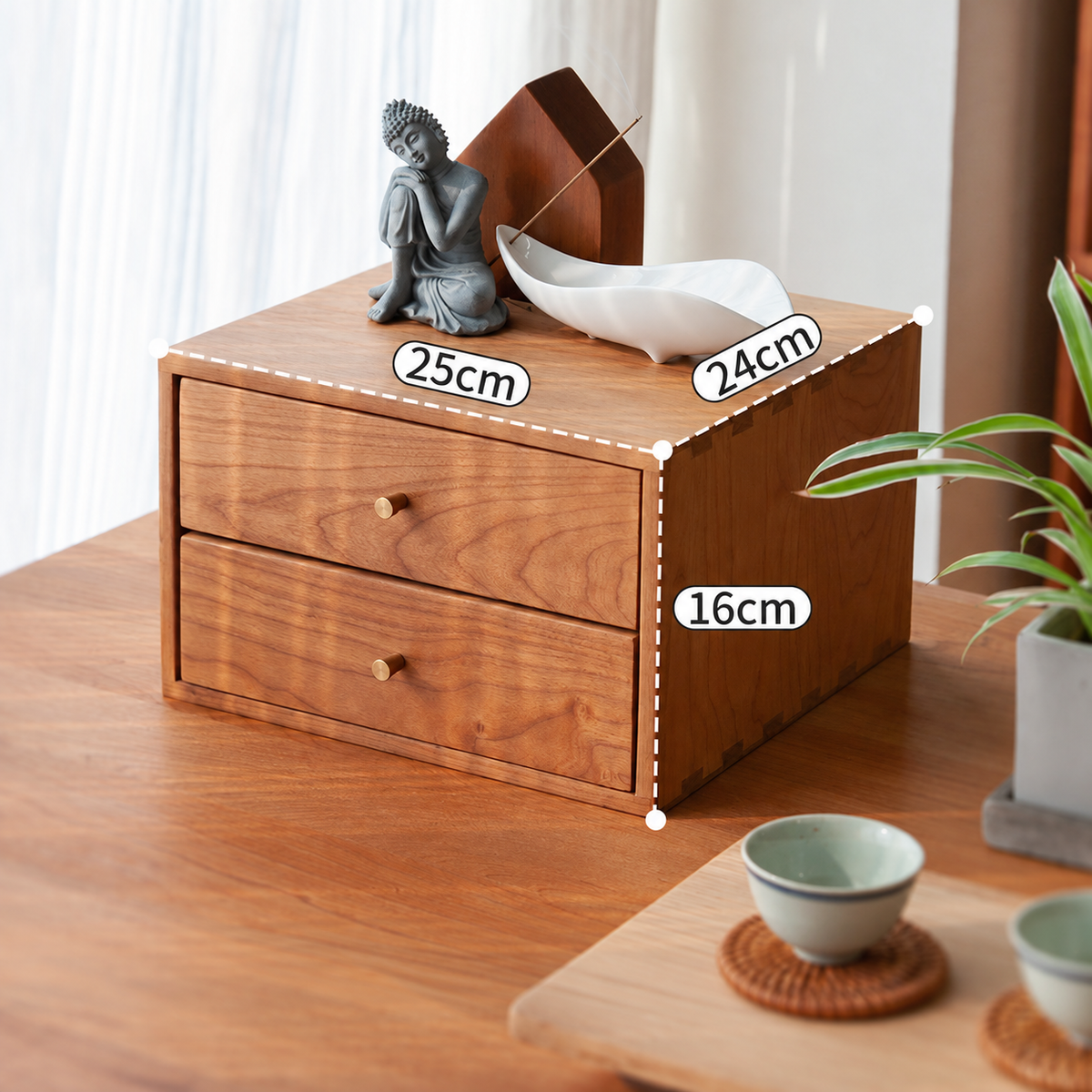 A wooden two-drawer organizer box with a warm medium-brown finish, shown on a wooden table with decorative items on top. White dimension labels reading 25cm, 24cm, and 16cm are overlaid on the box, along with a dashed outline indicating measurements.