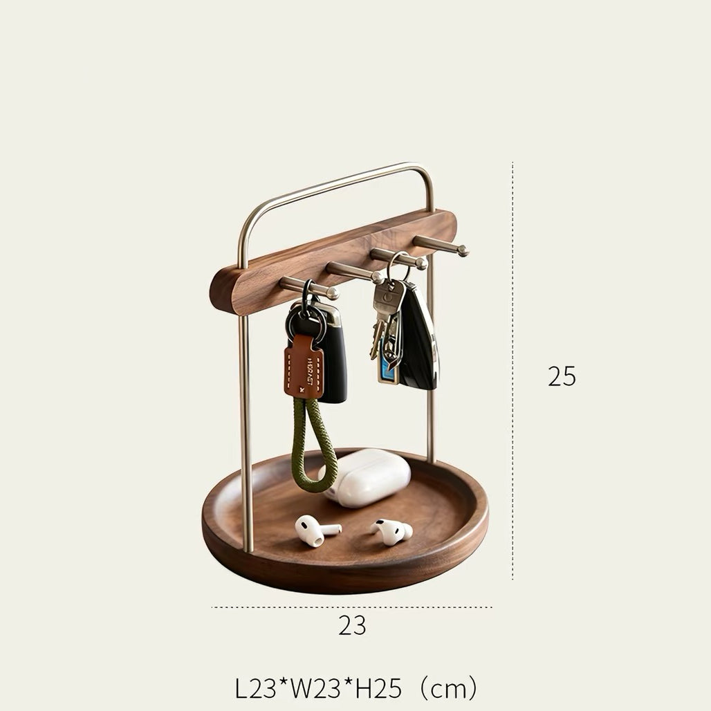 A wooden and metal key holder with a round tray, shown holding keys, a phone case, and earbuds. Dimension lines indicate a width of 23 cm and a height of 25 cm, with the full product labeled L23*W23*H25 (cm) at the bottom.
