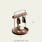 A wooden and metal key holder with a round tray, shown holding keys, a phone case, and earbuds. Dimension lines indicate a width of 23 cm and a height of 25 cm, with the full product labeled L23*W23*H25 (cm) at the bottom.