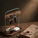A wooden and metal key holder with hooks, styled on a rustic wooden table with keys, a smartwatch, and earbud case resting on a matching tray, alongside a wood block with coffee beans.