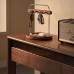 A wooden and metal key holder with hanging keys and a small tray holding earbuds, styled on a wooden desk next to a Marshall speaker.