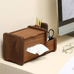 A dark brown wooden desk organizer with a tissue dispenser, pen holder, and small drawer, shown on a desk next to a computer monitor and eyeglasses.