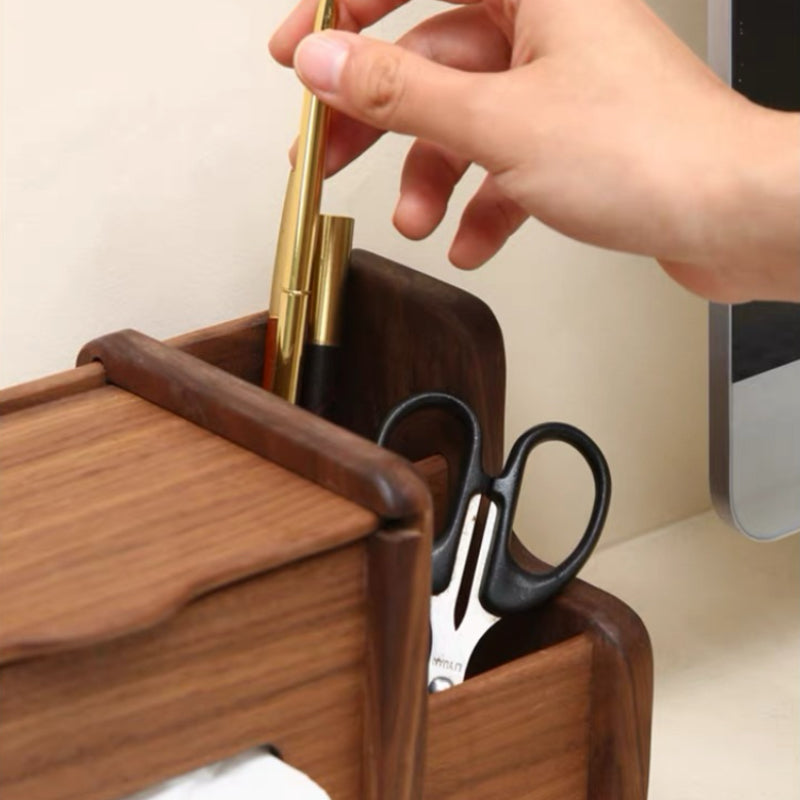A close-up of a wooden desk organizer holding pens and scissors, with a hand inserting a pen into the top compartment.