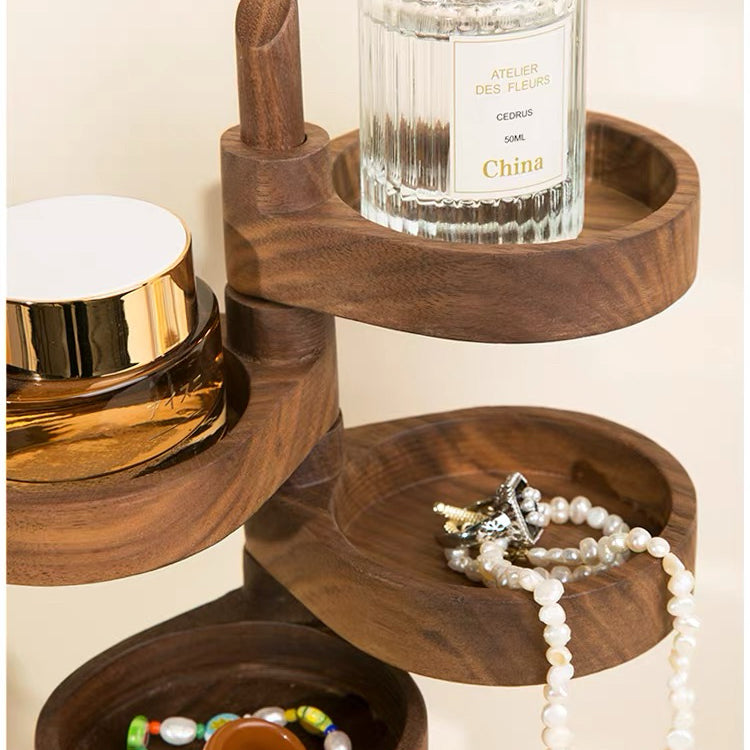 A dark brown wooden jewelry organizer with multiple tiers, styled with a perfume bottle, a gold-lidded jar, and pearl necklaces on its shelves.