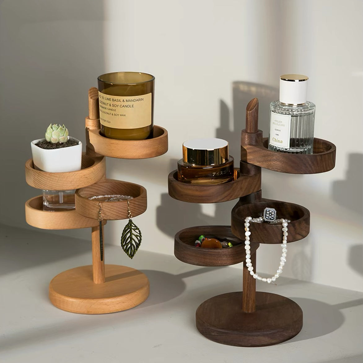 Two wooden jewelry and small-item organizers in different wood tones, styled with a candle, succulent, perfume bottle, cosmetics, earrings, rings, and a pearl necklace on a warm beige background.