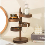 A dark brown wooden jewelry organizer stand with multiple tiers, styled on a tabletop next to a round mirror, a perfume bottle, and a candle.