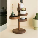 A wooden tiered organizer stand with a round base, shown holding a small vase, succulent, candle, and bottle. The stand is styled on a beige tabletop with a mirror and potted cactus in the background.
