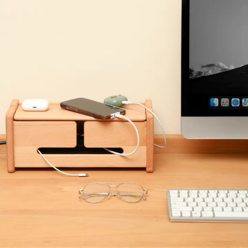 A light natural wood desktop organizer with two drawers and cable management slots, shown on a desk with a computer monitor, keyboard, glasses, and charging accessories.