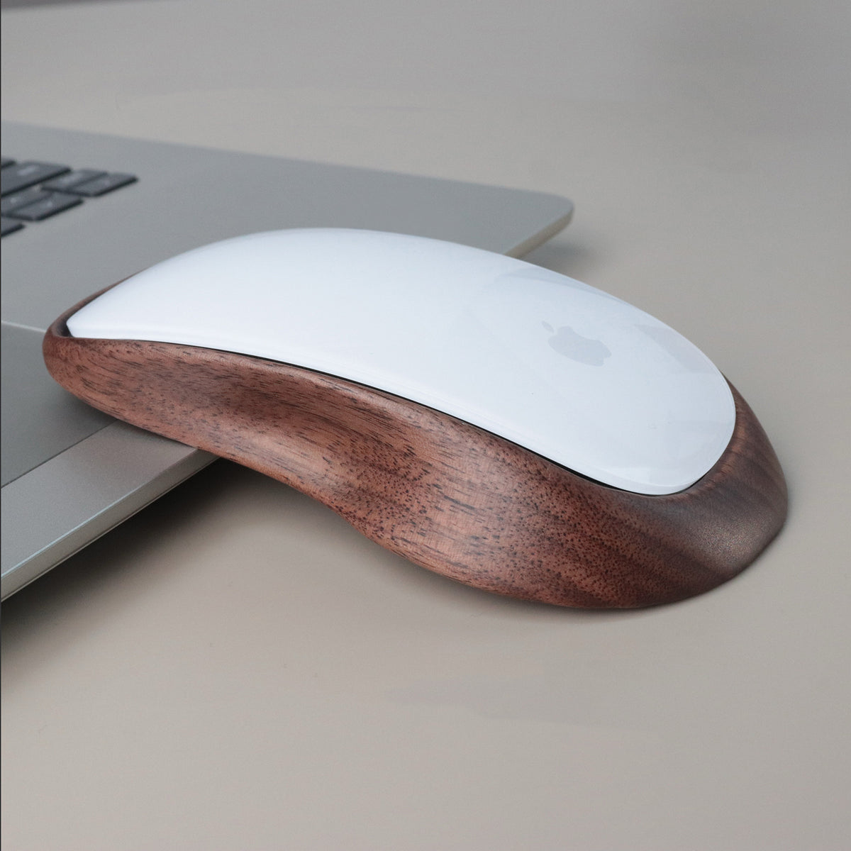 A wireless computer mouse with a glossy white top and a contoured dark brown wood-grain base, resting on a light gray surface next to a silver laptop.