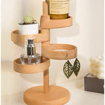 A light natural wood spiral jewelry organizer with multiple tiers, styled with a small succulent, a perfume bottle, a candle, and a pair of dangling leaf earrings against a warm cream background.