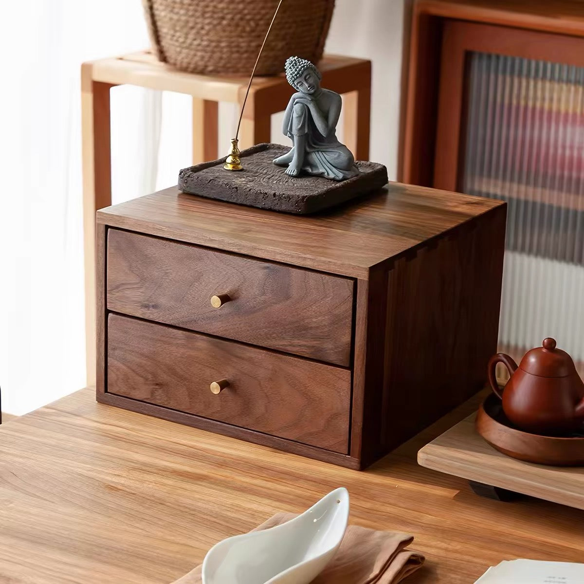A dark brown wooden two-drawer organizer box with brass knobs, styled on a wooden table in a warm, home-like setting with a small Buddha figurine on top.