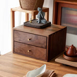 A dark brown wooden two-drawer organizer box with brass knobs, styled on a wooden table in a warm, home-like setting with a small Buddha figurine on top.