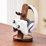 A wooden game controller stand holding a white game controller and a white over-ear headset, placed on a wooden table in a softly lit indoor setting.