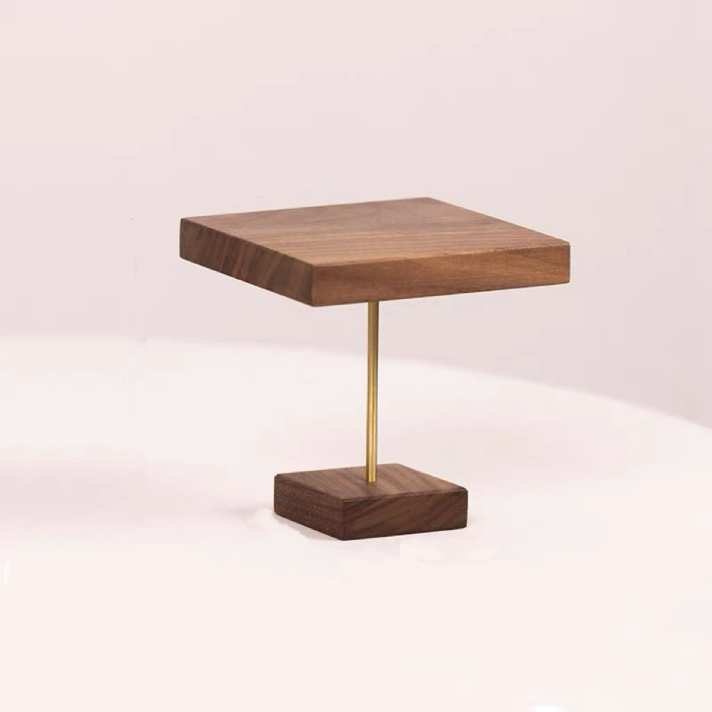 A modern square wooden side table with a dark walnut finish and a slim brass metal pedestal base, shown on a clean white surface against a light pink background.
