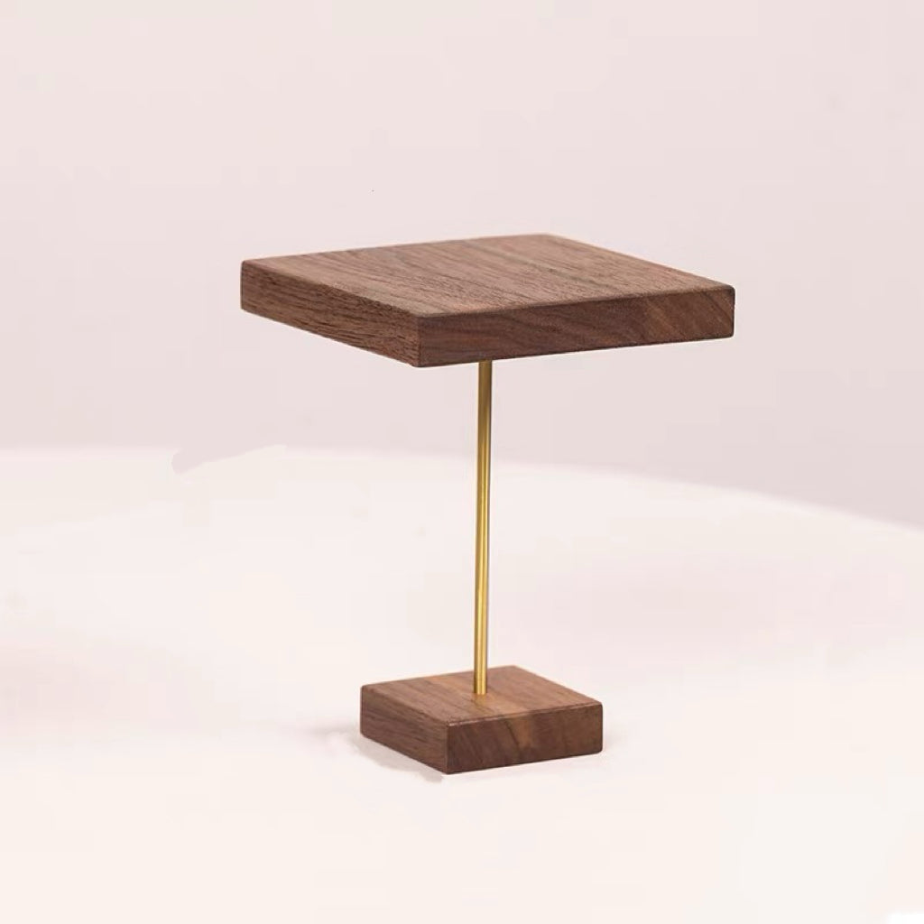 A modern square wooden tabletop on a slim gold metal stand, set against a clean, light beige background.
