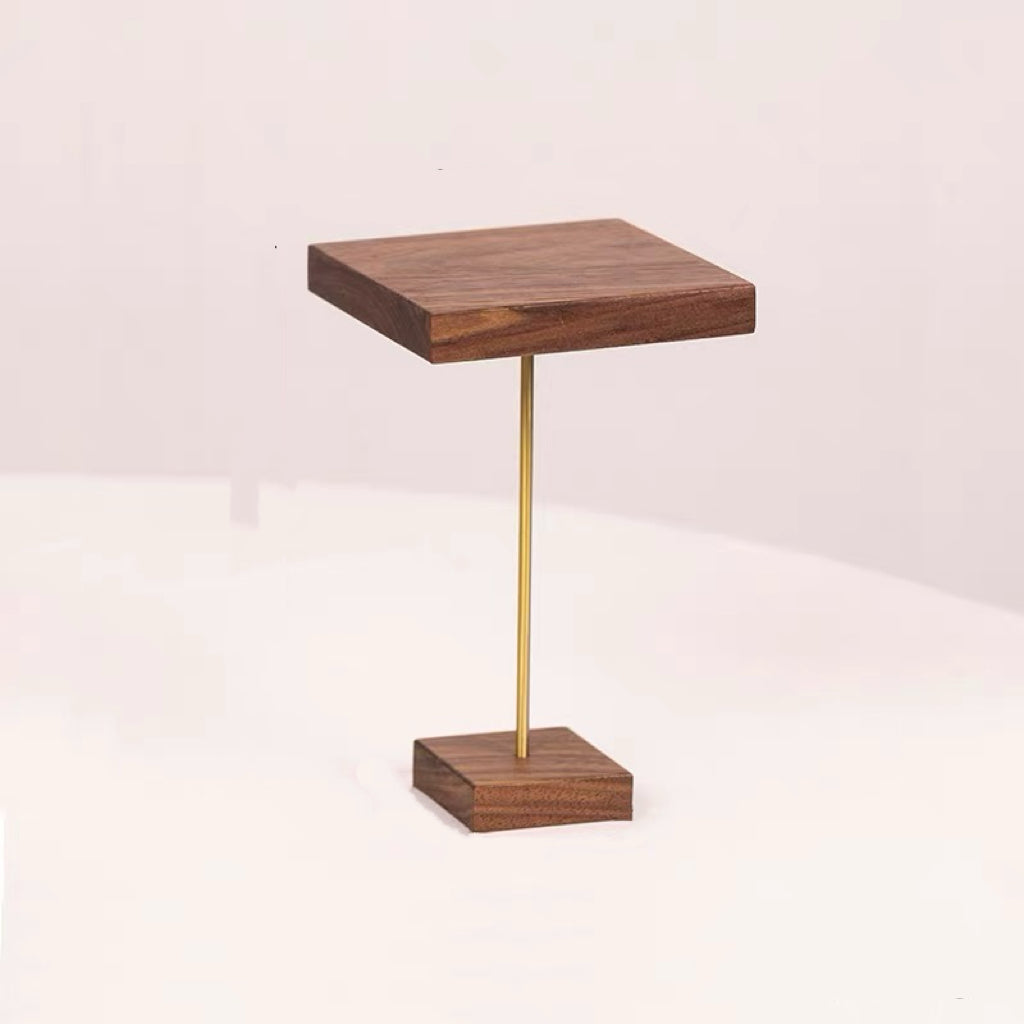 A modern side table featuring a square dark wood top and base with a slim vertical brass stand in the center, set against a plain light background.
