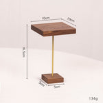 A small wooden tabletop display stand with a square dark wood top and base, a slim gold metal center rod, and dimension callouts showing 10 cm top, 16.5 cm height, 5 cm base, and 134 g weight on a light neutral background.