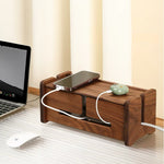 A dark brown wooden desktop organizer with drawers and a top tray, shown on a desk with a laptop, mouse, and phone plugged in. The background features cream-colored vertical blinds.