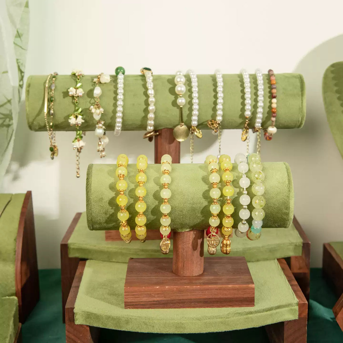 A display stand holding multiple beaded bracelets and bangles in green, yellow, white, and gold tones, photographed indoors against a light wall.
