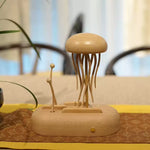 A light natural wood decorative sculpture resembling a jellyfish with long tentacles on a matching oval base, placed on a patterned surface in a softly blurred indoor setting.