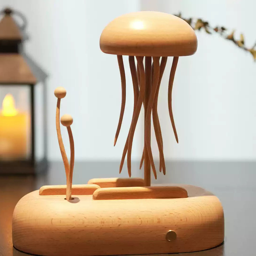 A wooden jellyfish-shaped decorative object with long tentacles on a matching base, displayed on a tabletop with a blurred lantern candle and plant in the background.