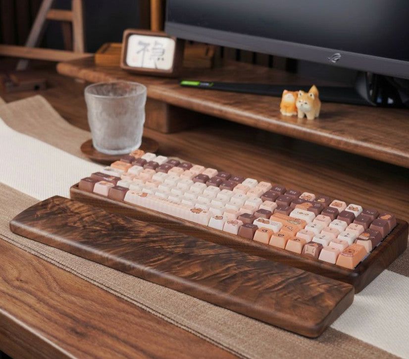 A wooden mechanical keyboard with pastel-colored keycaps and a matching wooden wrist rest, styled on a desk shelf in front of a computer monitor.