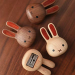 Four wooden rabbit-shaped pencil sharpers arranged on a dark wood tabletop, showing both front and back views with different natural wood tones and reddish-brown inlay details.