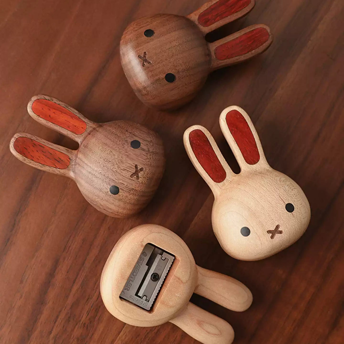 Four wooden rabbit-shaped pencil sharpers arranged on a dark wood tabletop, showing both front and back views with different natural wood tones and reddish-brown inlay details.